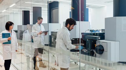 Due scienziati in camice bianco che lavorano in un laboratorio di fronte ad un grande strumento analitico rettangolare 